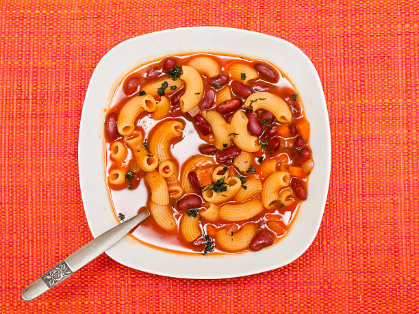 A spoon lifting Pasta Fagioli from a bowl, showing beans, pasta, and broth.