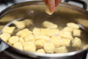  Hands placing fresh dumplings into a pot of water.