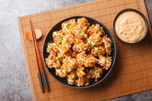 Crispy Bang Bang Chicken with creamy dipping sauce and chopsticks on a bamboo mat