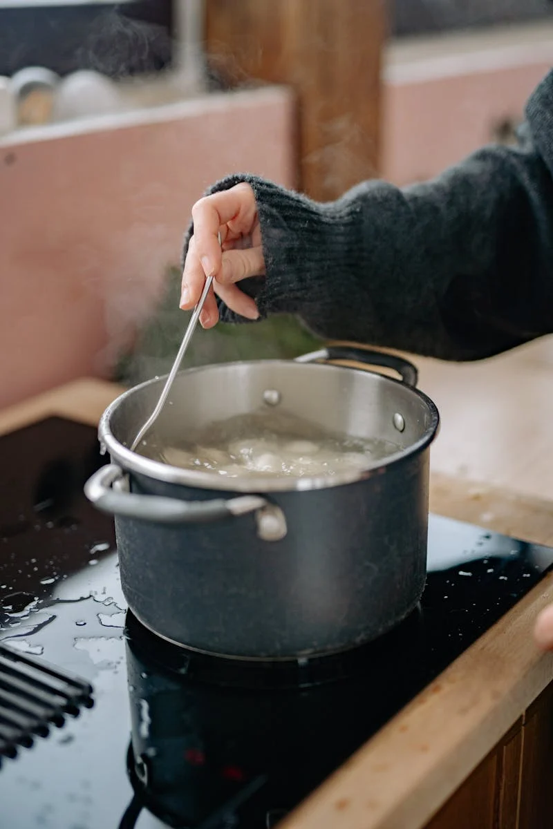 A pot of dumplings boiling in water with steam rising.