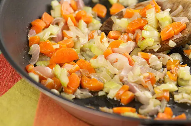 Chopped onions, carrots, celery, and garlic being sautéed in a pot