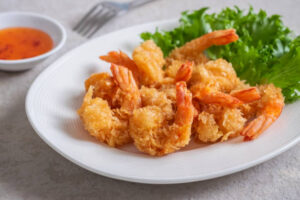 Crispy fried shrimp served on a white plate with lettuce garnish and dipping sauce in the background