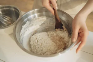 Hands mixing biscuit dough with a wooden spoon in a bowl.