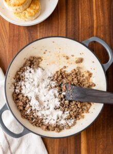  Flour being stirred into sausage fat in a skillet to create a smooth roux for gravy.