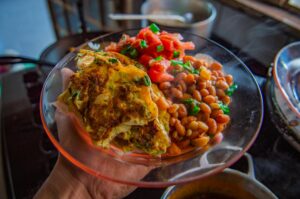 A vibrant dish featuring seasoned beans with fresh tomatoes, herbs, and a golden-brown omelet served on a glass plate.