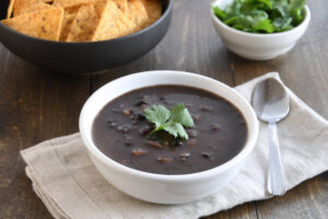 A bowl of black bean soup garnished with fresh cilantro, served with tortilla chips and a side of fresh herbs.