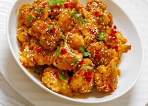 Vegan Bang Bang Cauliflower with sesame seeds and fresh herbs on a white plate