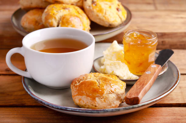 Freshly baked biscuit served with tea, butter, and jam on a rustic wooden table.