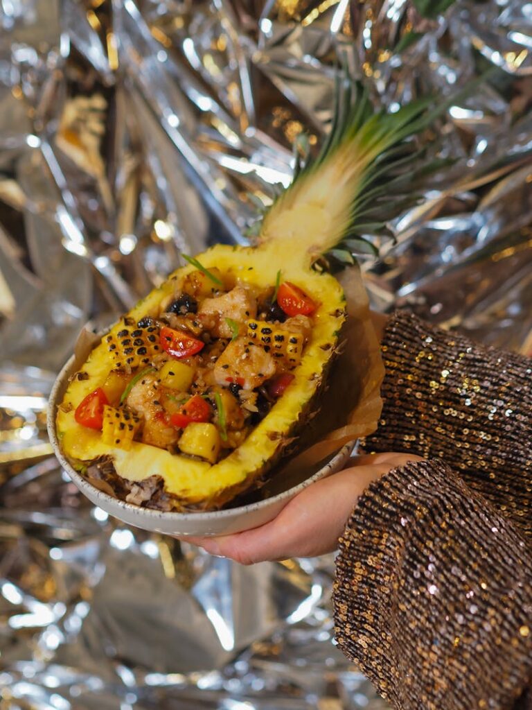 A hollowed-out pineapple filled with grilled fruits, vegetables, and shrimp, garnished with fresh herbs, a tropical pairing for shrimp dishes.