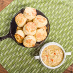 Freshly baked biscuits and dumplings in a bowl of soup on a wooden table.