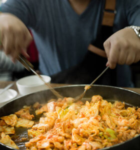 Chef stir-frying shrimp and vegetables in a large skillet