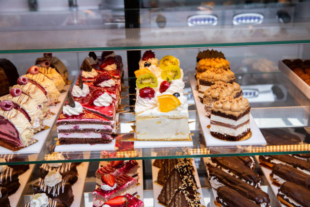 Display of assorted cakes and desserts in a bakery, including layered cakes and cream-filled pastries.