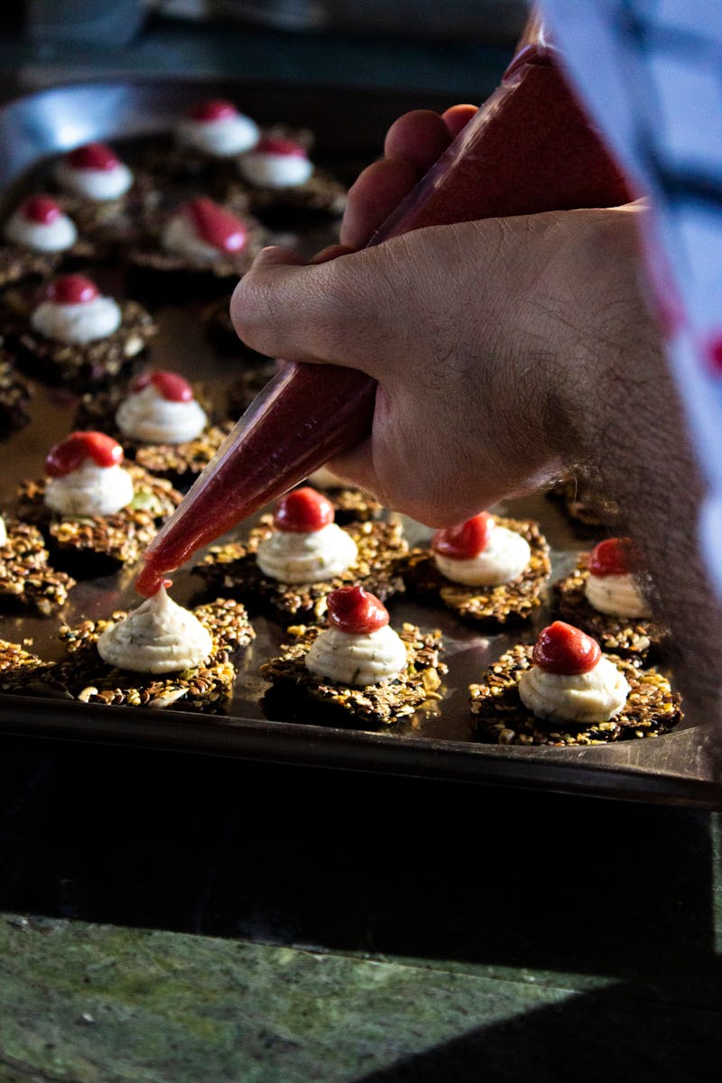 A chef piping cream onto individual cheesecake bites with precision, highlighting the art of cheesecake preparation.