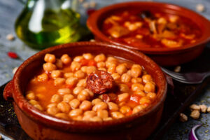 "Pinto beans in a rich tomato-based sauce with sausage in a clay bowl