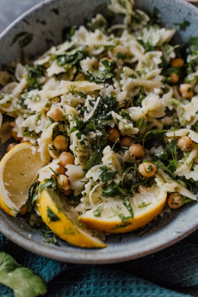 Close-up of a chickpea pasta salad garnished with fresh herbs, lemon slices, and Parmesan cheese.