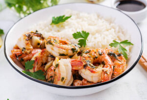 A bowl of coconut rice served with grilled shrimp, garnished with fresh parsley, creating a flavorful and tropical side dish for seafood