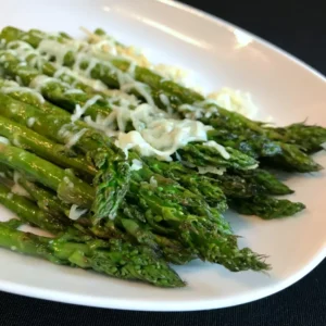  Grilled asparagus topped with melted parmesan cheese, served on a white plate, perfect as a side dish for shrimp