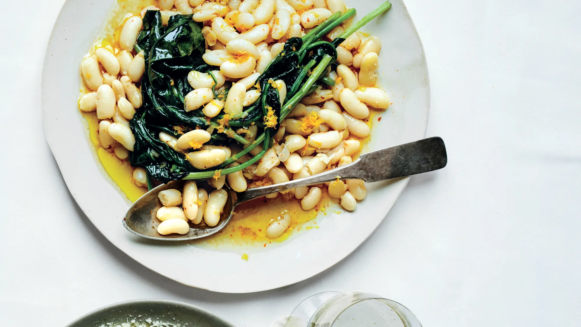 A plate of white beans seasoned with olive oil, garlic, and citrus zest, garnished with wilted greens, showcasing the best seasoning for beans