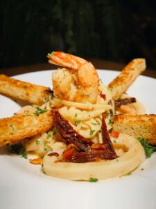 A plate of creamy pasta topped with grilled shrimp, sun-dried tomatoes, and served with crusty garlic bread, a perfect side dish for shrimp.