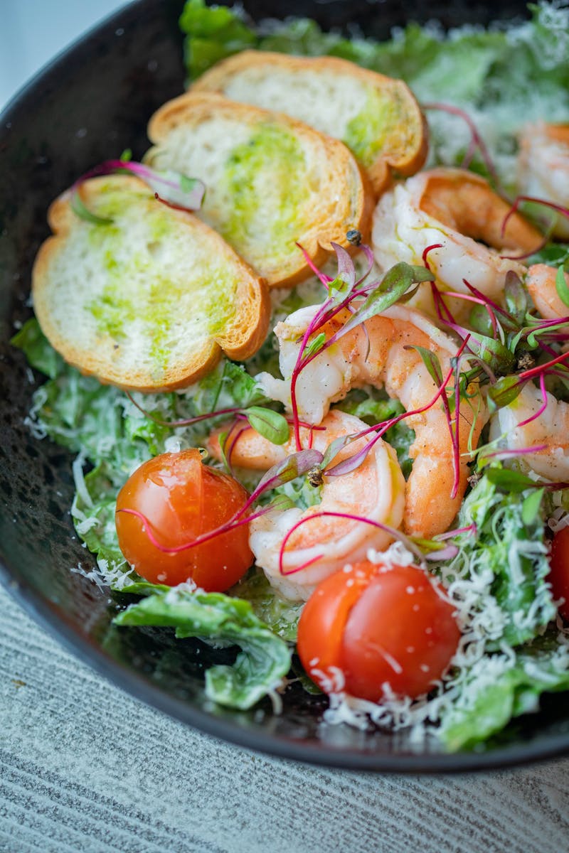 Fresh shrimp salad with cherry tomatoes, crisp greens, toasted bread slices, and garnished with microgreens.