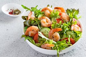 Fresh shrimp salad with mixed greens, cucumber, tomato slices, and a side of seasoning.