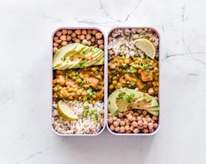 Vegan bean bowl with chickpeas, rice, avocado slices, and curry garnished with cilantro and lime