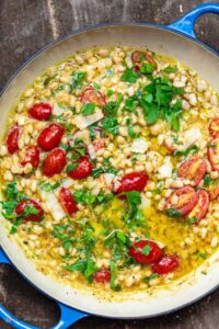 A skillet of creamy white beans with cherry tomatoes, fresh parsley, and olive oil, garnished with Parmesan cheese.