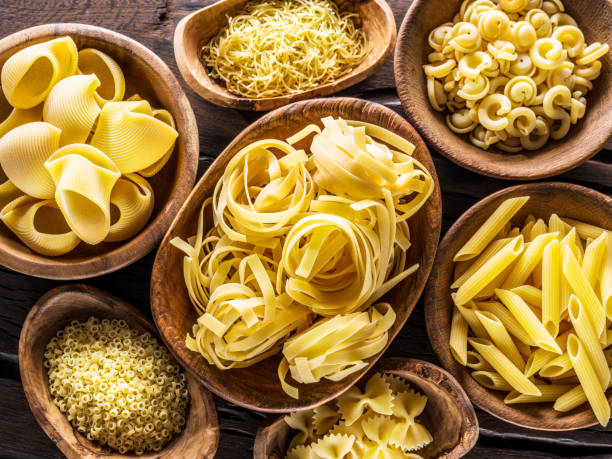 Various pasta types including fettuccine, penne, and pappardelle on a wooden board