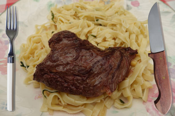 A plate of steak pasta with creamy Alfredo sauce, garnished with fresh herbs