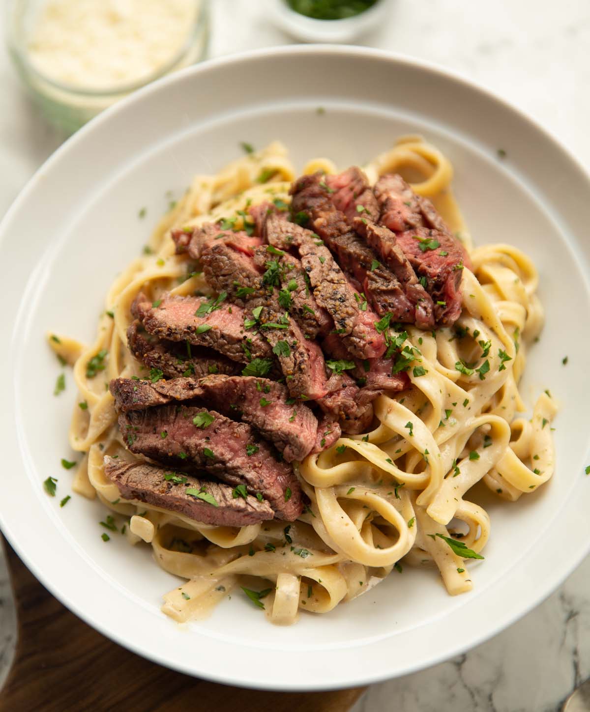 Creamy steak pasta with fettuccine and sliced ribeye steak in a white bowl